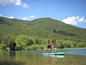 Ein Paar paddelt auf einem Stand Up Paddle Board auf einem See mit einem grünen Hügel im Hintergrund.