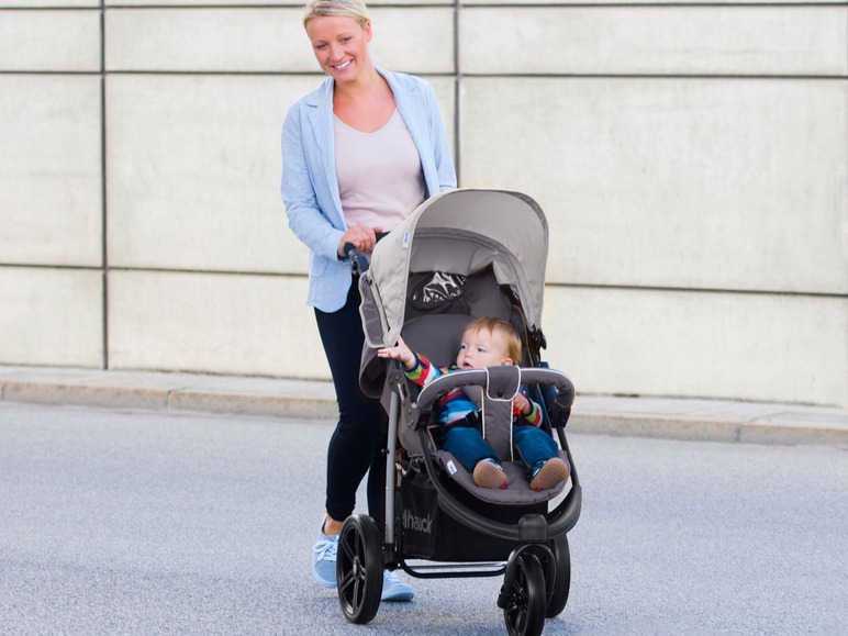 Eine Frau schiebt einen Hauck Kinderwagen mit einem Baby auf der Straße.
