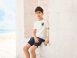 Ein Junge trägt ein weißes T-Shirt mit Aufdruck und blaue Jeans-Shorts.