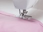Eine Nähmaschine näht rosafarbenen Stoff mit einem Rollfuss.
