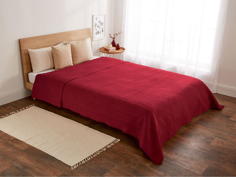 Eine bordeauxrote Tagesdecke mit einem detaillierten Steppmuster auf einem Bett mit Kissen.