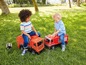 Zwei Kinder spielen mit einem roten Müllwagen und einem Feuerwehrauto im Garten.