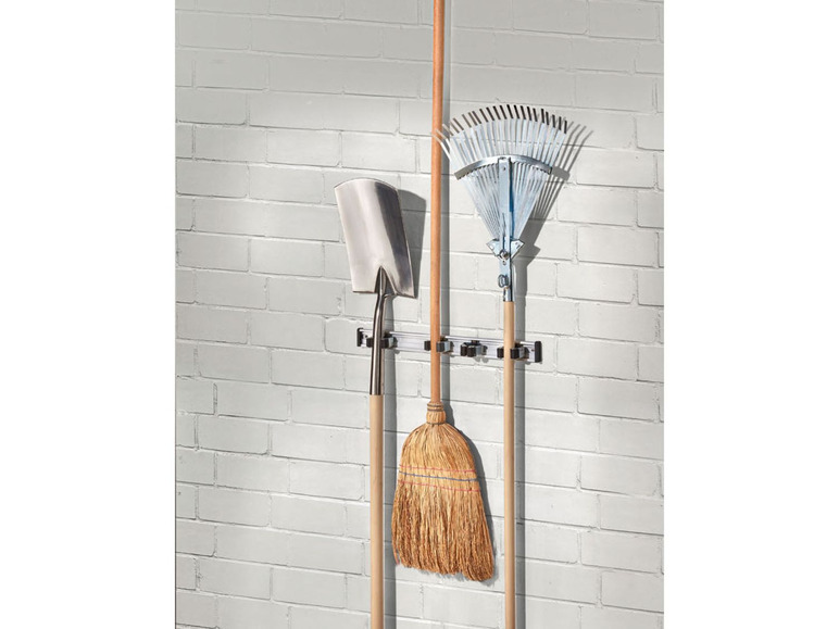 Ein Besen, eine Schaufel und eine Harke hängen an einer Wandhalterung.