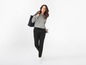 Eine Frau trägt einen grauen Pullover, eine schwarze Hose und eine schwarze Tasche.