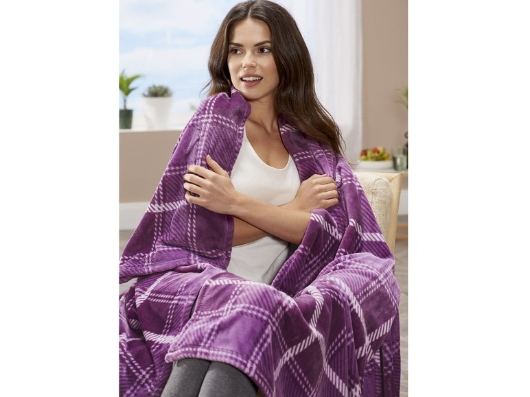 Eine Frau sitzt auf einem Stuhl mit einer karierten lila Decke.