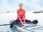 Eine Frau sitzt auf einem Paddleboard im Meer mit einem Paddel.