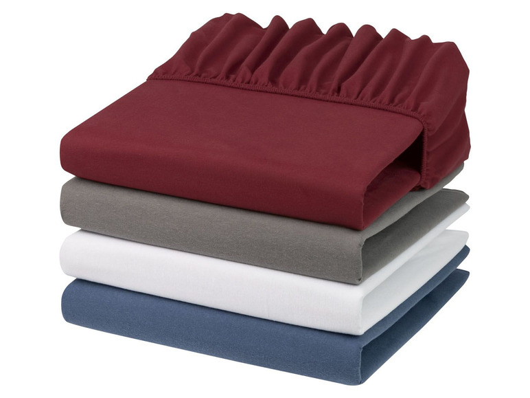 Stapel Bettwäsche in verschiedenen Farben, darunter Rot, Grau, Weiß und Blau.