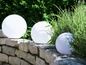 Drei runde weiße Gartenleuchten auf einer Steinmauer.