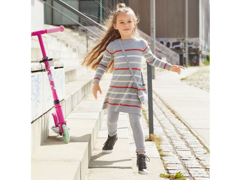 Ein Mädchen in einem gestreiften Kleid und Leggings mit einem rosafarbenen Roller.