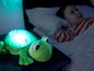 Ein grünes Frosch-Nachtlicht mit Sternenprojektion und einem Kind im Bett.