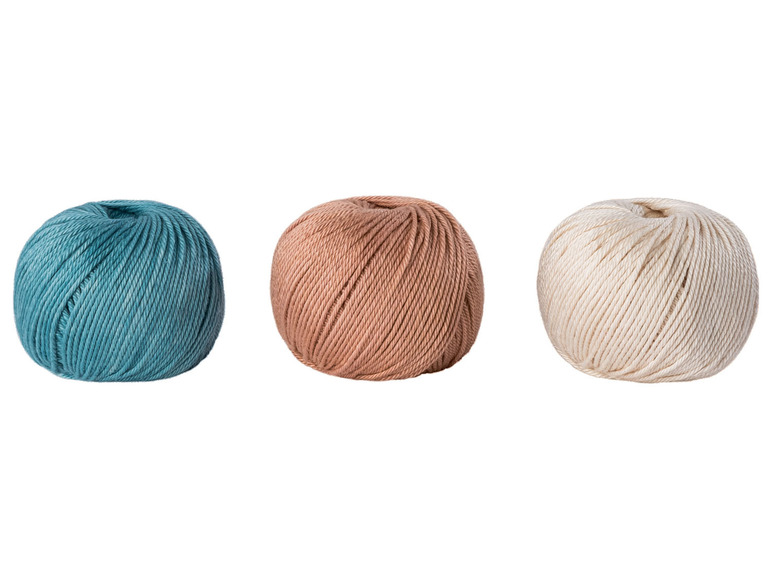 Drei Knäuel Garn in blau, beige und weiß.