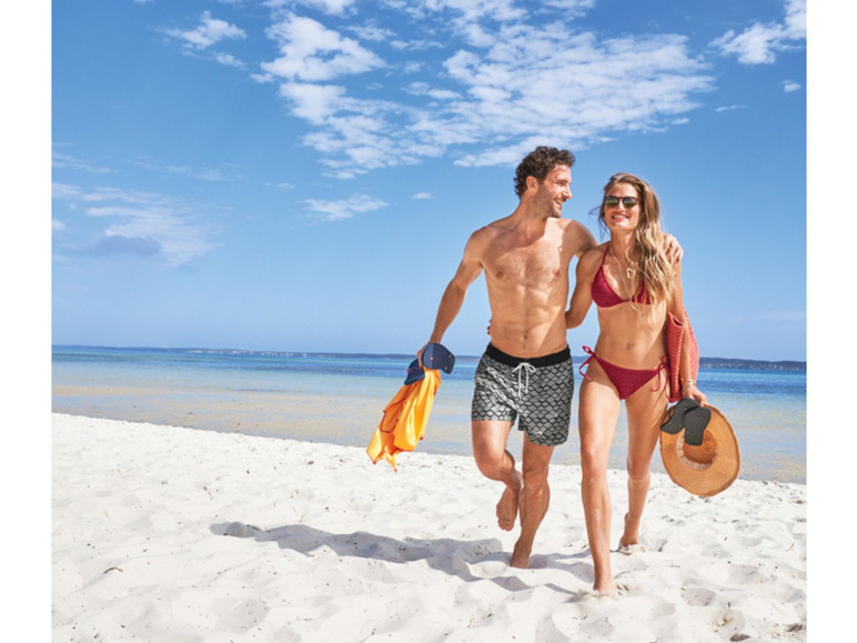 Ein Paar in Badekleidung geht über einen weißen Sandstrand.