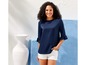 Eine Frau trägt eine dunkelblaue Bluse mit Rüschenärmeln und weiße Shorts.
