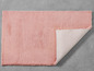 Ein rosa Plüschteppich mit sichtbarer rutschfester Unterseite.