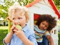 Zwei Kinder spielen in einem Spielhaus von Smoby, eines von ihnen isst einen Apfel.