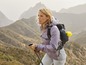 Eine Frau mit Rucksack und Wanderstöcken geht durch eine Berglandschaft.