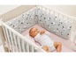 Baby in einem Gitterbett mit einem grauen und weißen Gitterbett-Schutz mit Schafen.
