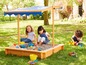 Kinder spielen in einem Sandkasten mit Sonnenschutz.