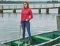 Eine Frau in einem roten Pullover, blauen Jeans und braunen Stiefeln steht auf einem Boot.