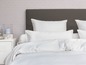 Weiße Bettwäsche mit Kissen auf einem Bett mit dunkelgrauem Kopfteil.