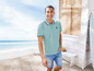 Mann in blauem Poloshirt und Shorts am Strand.