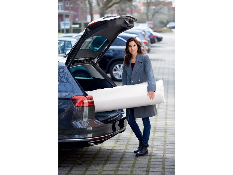 Eine Frau legt eine Matratze in den Kofferraum eines Autos.