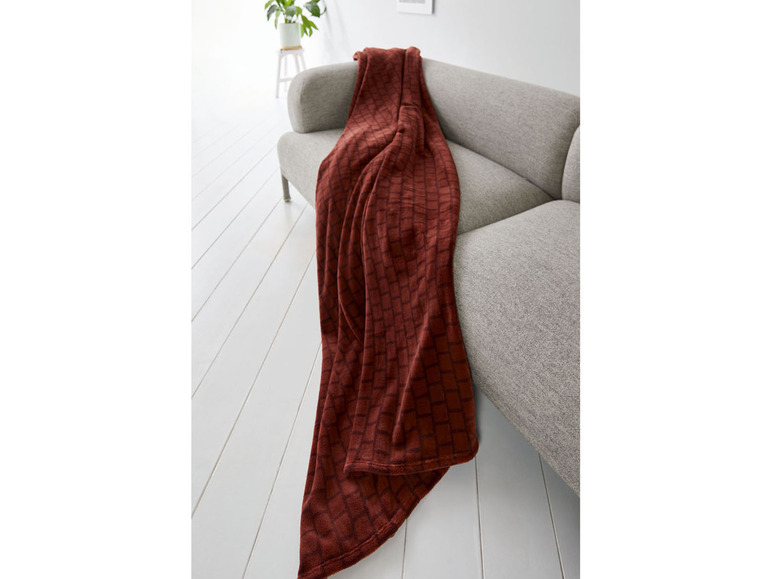 Eine dunkelrote Plaid mit Karomuster auf einer grauen Couch.