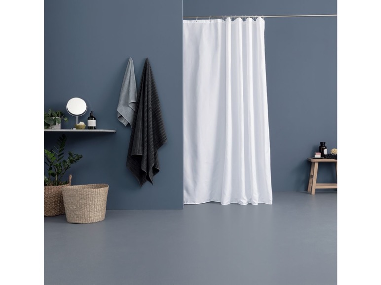 Ein weißer Duschvorhang, zwei Handtücher und ein Badezimmerkorb in einem blauen Badezimmer.