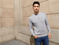 Mann in einem grauen Pullover mit Zopfmuster und blauen Jeans.
