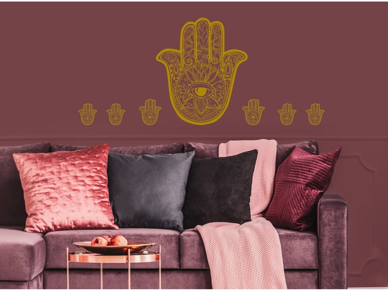 Große und kleine Hamsa-Aufkleber an einer rosa Wand über einem Sofa.