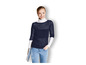 Eine Frau in einem dunkelblauen Pullover mit durchbrochenen Details und blauen Jeans.