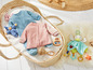 Babykleidung, darunter ein rosa und ein blauer Strampler, in einem Weidenkorb.