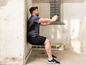Mann in Sportkleidung macht Squats an einer Wand.