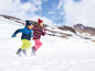 Zwei Kinder in Winterkleidung rennen durch den Schnee in den Bergen.