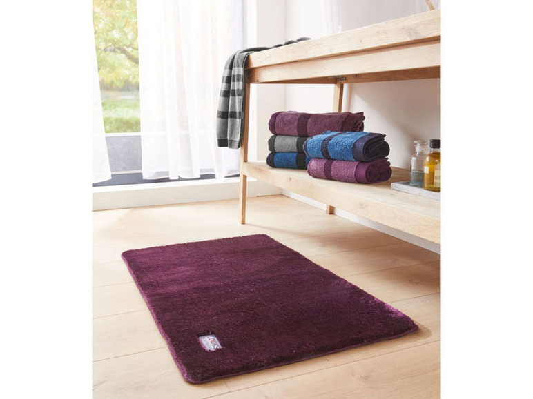 Eine lila Badematte und Handtücher auf einem Holzregal.