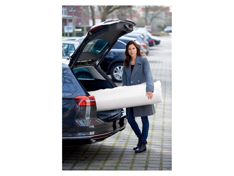 Eine Frau lädt eine Matratze in den Kofferraum eines Autos.