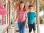 Zwei Kinder in legerer Kleidung, ein Junge mit einem blauen 'Surfing'-Shirt und ein Mädchen mit einem rosafarbenen 'What a Perfect Day'-Shirt.