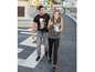 Ein Mann und eine Frau gehen auf der Straße, er trägt ein schwarzes T-Shirt mit Aufdruck und graue Jogginghosen, sie trägt eine schwarze Bluse mit Tiermuster und schwarze Leggings.