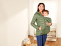 Eine Frau trägt ein Baby in einer Trage und trägt eine grüne Winterjacke.
