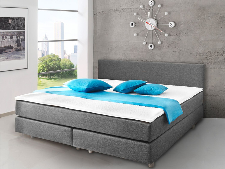 Ein graues Boxspringbett mit blauen Kissen.