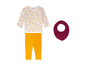 Ein Baby-Set mit Lupilu Langarmshirt mit Blumenmuster, gelben Leggings und einem rosafarbenen Lätzchen.