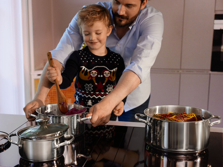 Ein Vater und sein Sohn kochen zusammen in der Küche mit Töpfen und einem Holzlöffel.