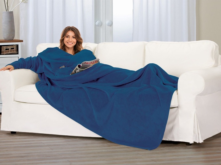 Eine Frau trägt eine blaue Fleece-Decke mit Ärmeln auf der Couch.