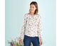 Frau in einer weißen Bluse mit Blumenmuster und blauen Jeans.