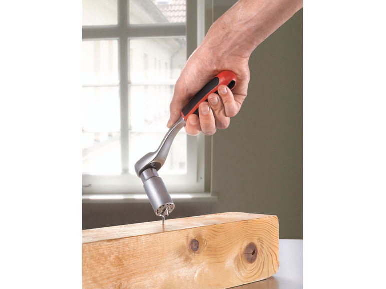 Eine Hand hält eine Ratsche mit Bit-Satz, um eine Schraube in Holz zu drehen.