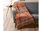 Eine gestreifte Decke in Orange-, Rot- und Grüntönen auf einem grauen Sofa.