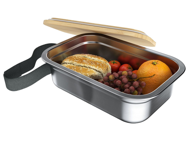 Eine Edelstahl-Lunchbox mit Holzdeckel, gefüllt mit Brot, Trauben und einer Orange.
