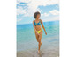 Eine Frau in einem blauen Bikini mit tropischem Muster geht am Strand entlang.