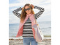 Frau in einer rosa Weste, einem gestreiften Oberteil und Jeans am Strand.