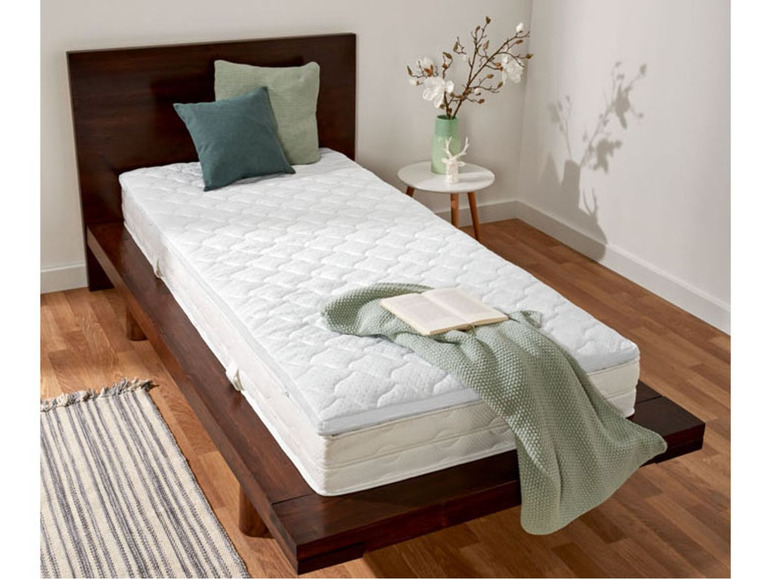 Eine weiße Matratze auf einem Holzbettgestell mit einer grünen Decke.